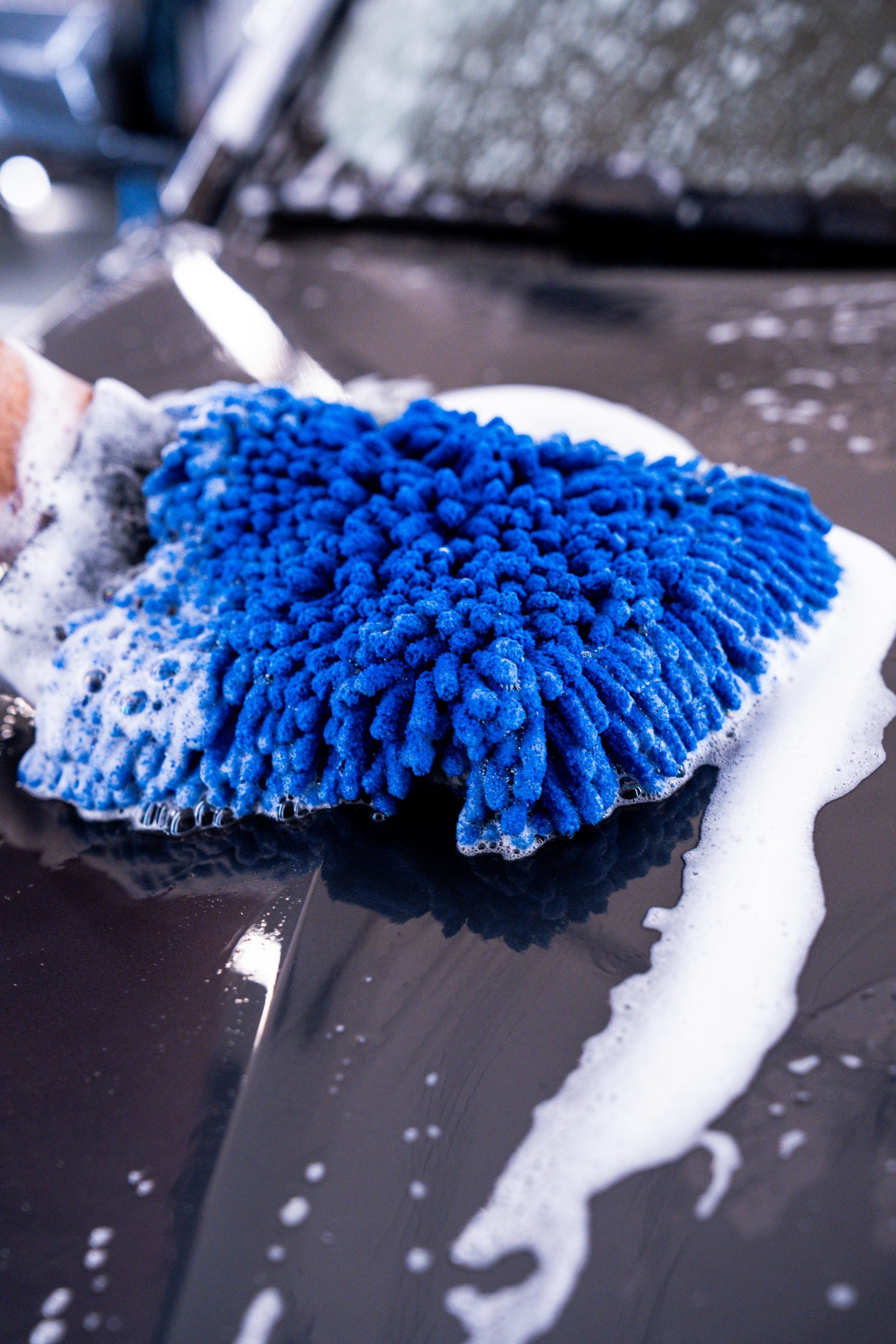 Car washing with a blue microfiber mitt on a soapy car surface