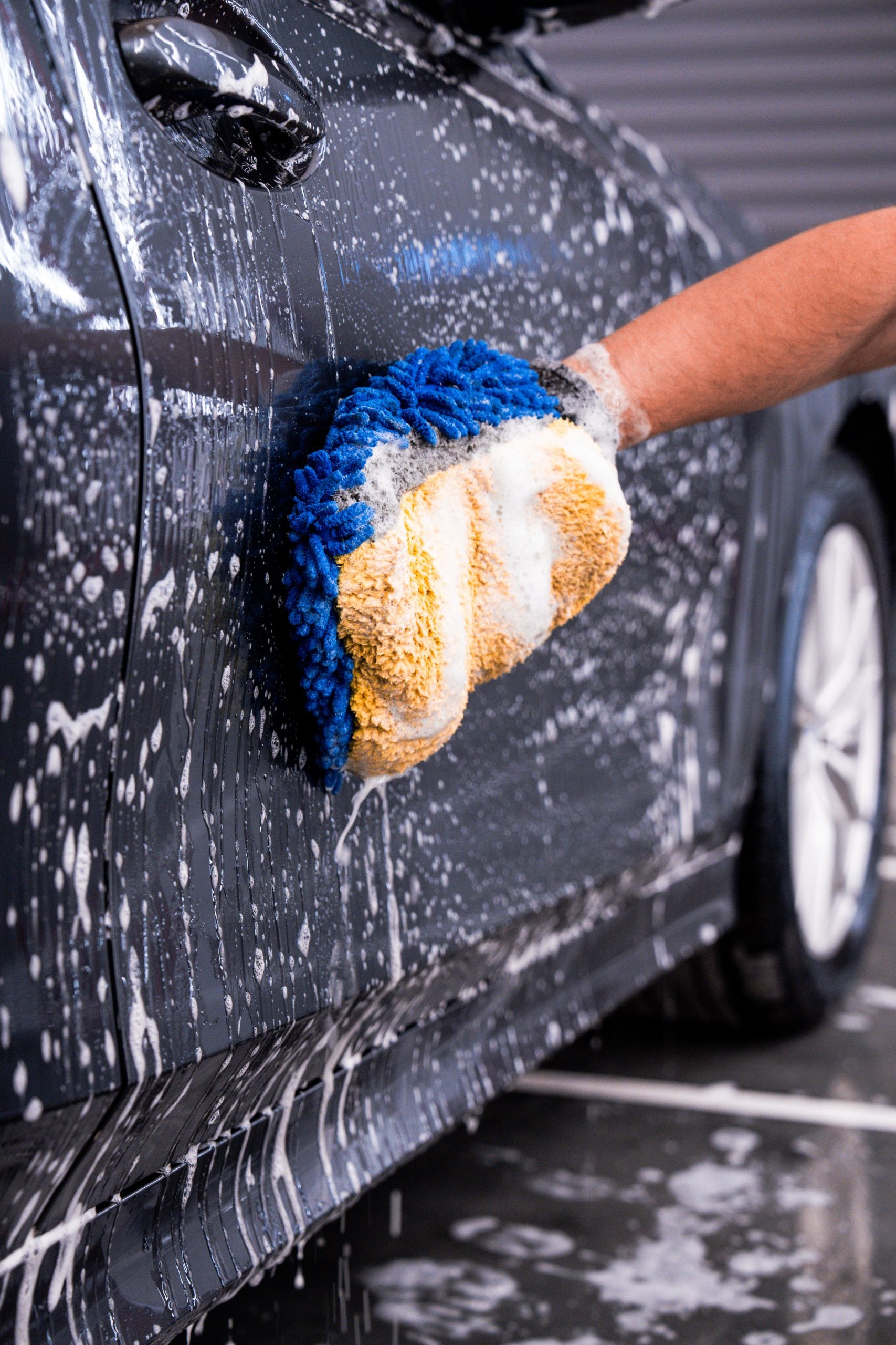 Person washing a car with a blue and orange sponge