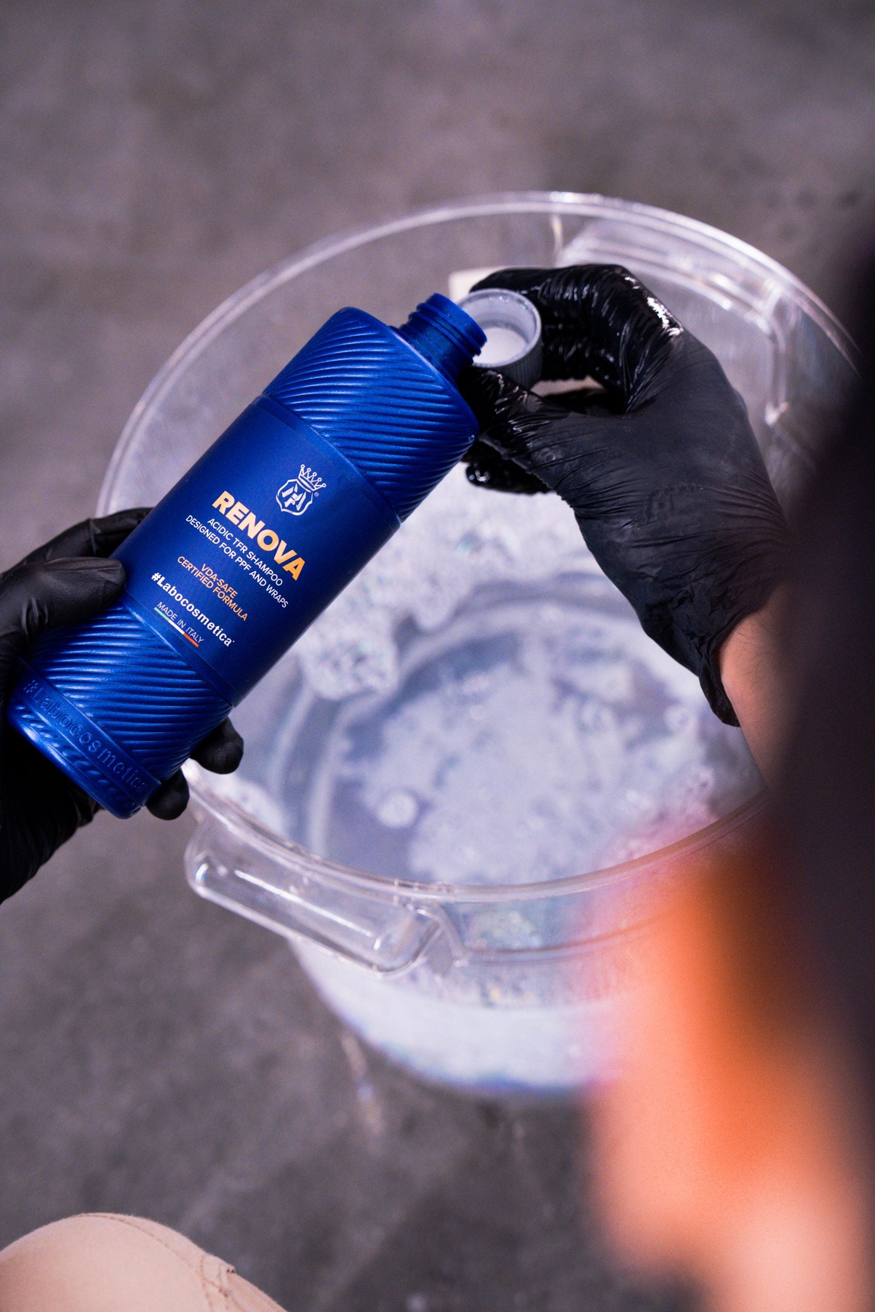Person holding a blue bottle labeled 'Renova' over a bucket with soapy water.