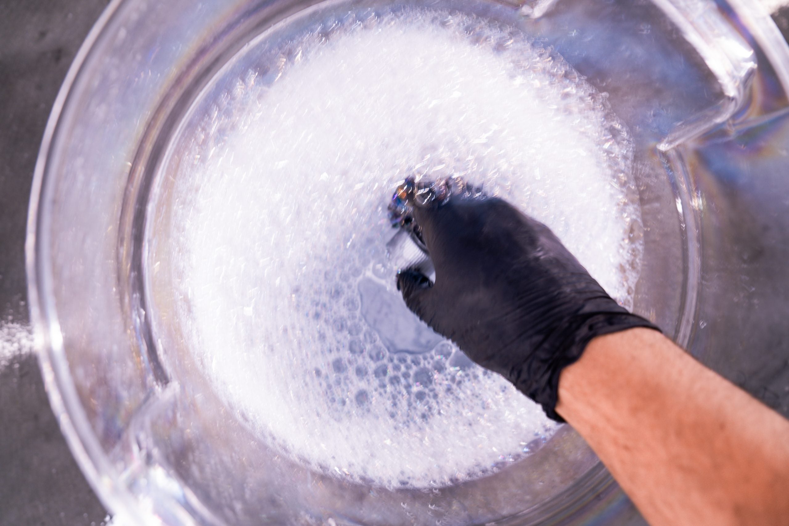 Hand wearing a black glove cleaning a metallic surface with soap bubbles.