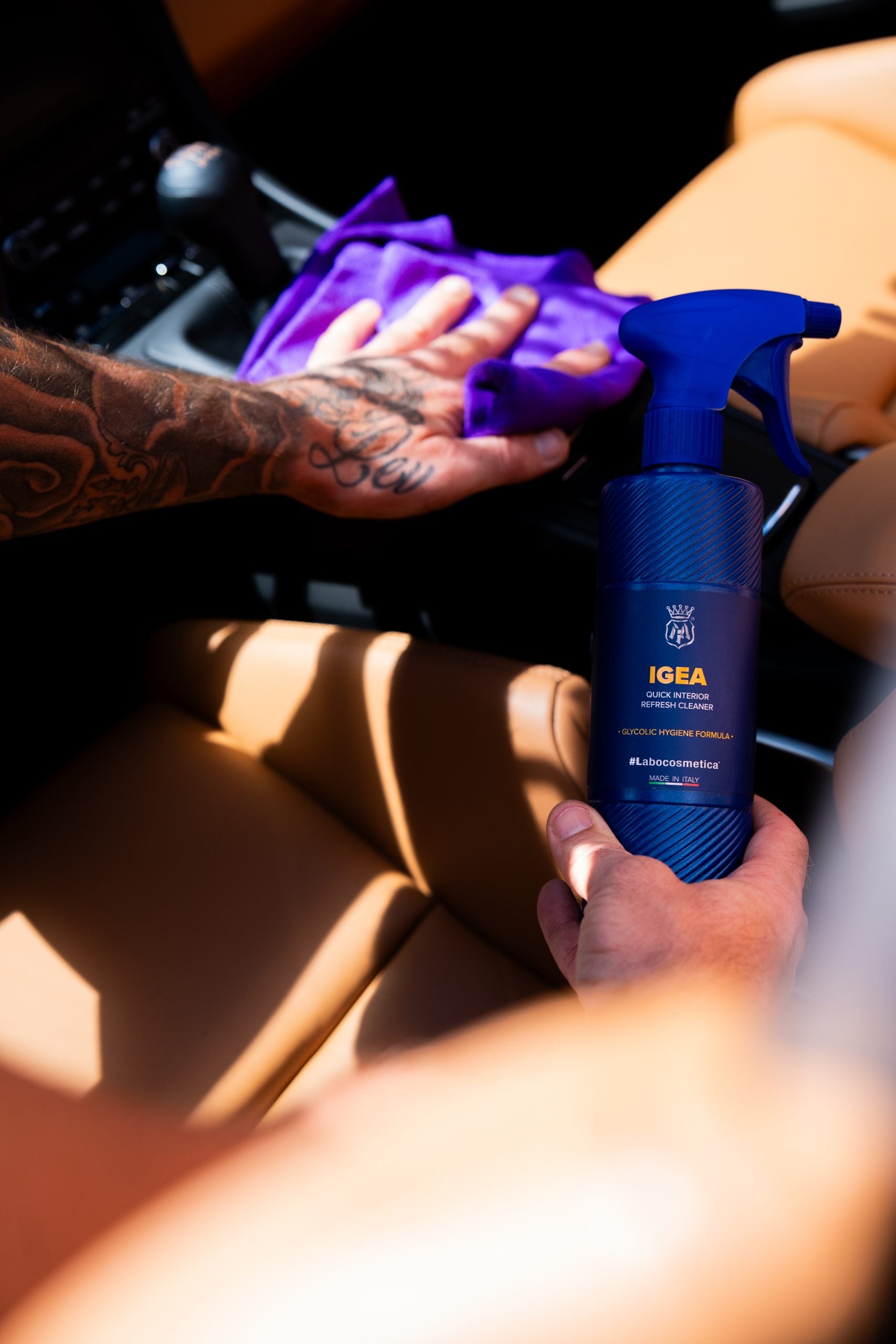 Person holding a blue spray bottle labeled 'IGEA' in a car.