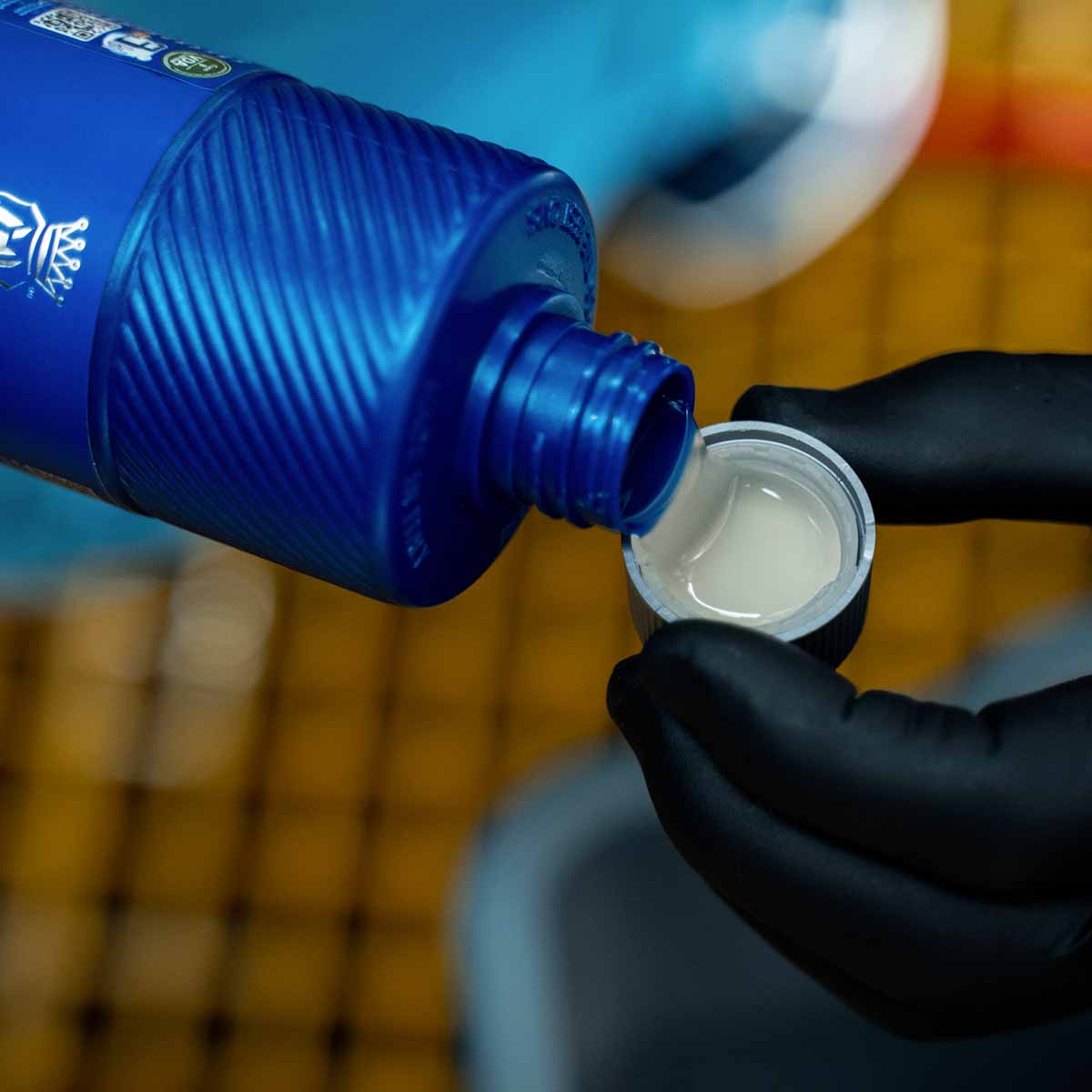 A hand in black gloves pouring Labocosmetica Sèmper car shampoo from a blue bottle into its cap, showing its concentrated formula.