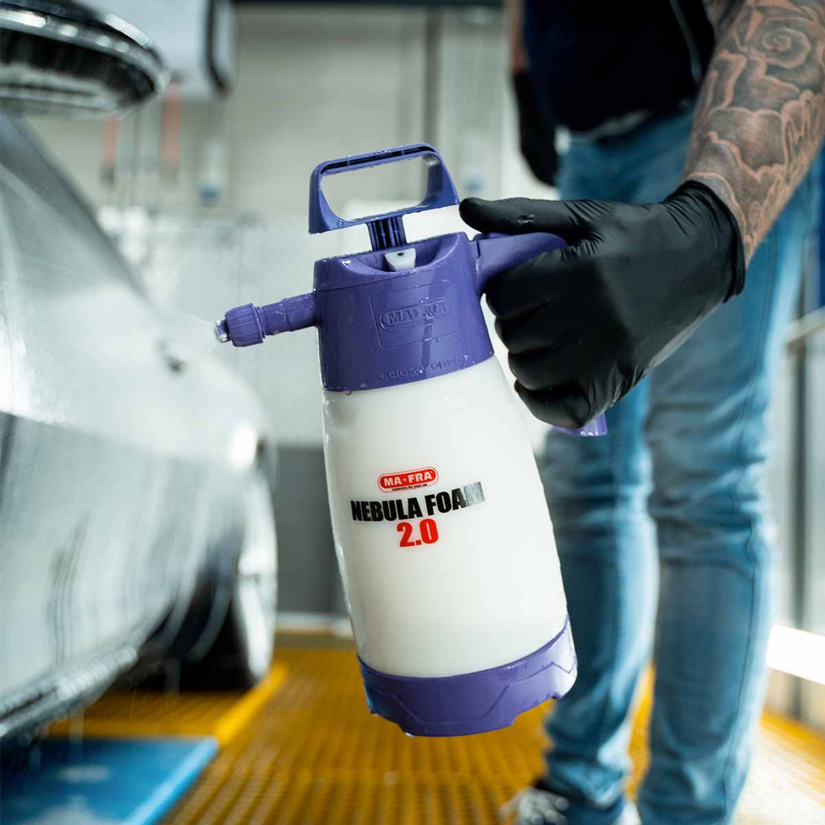 A car detailer holding a Ma-Fra Nebula foam sprayer to apply a thick layer of Labocosmetica Revitax foam to the side of a white car.