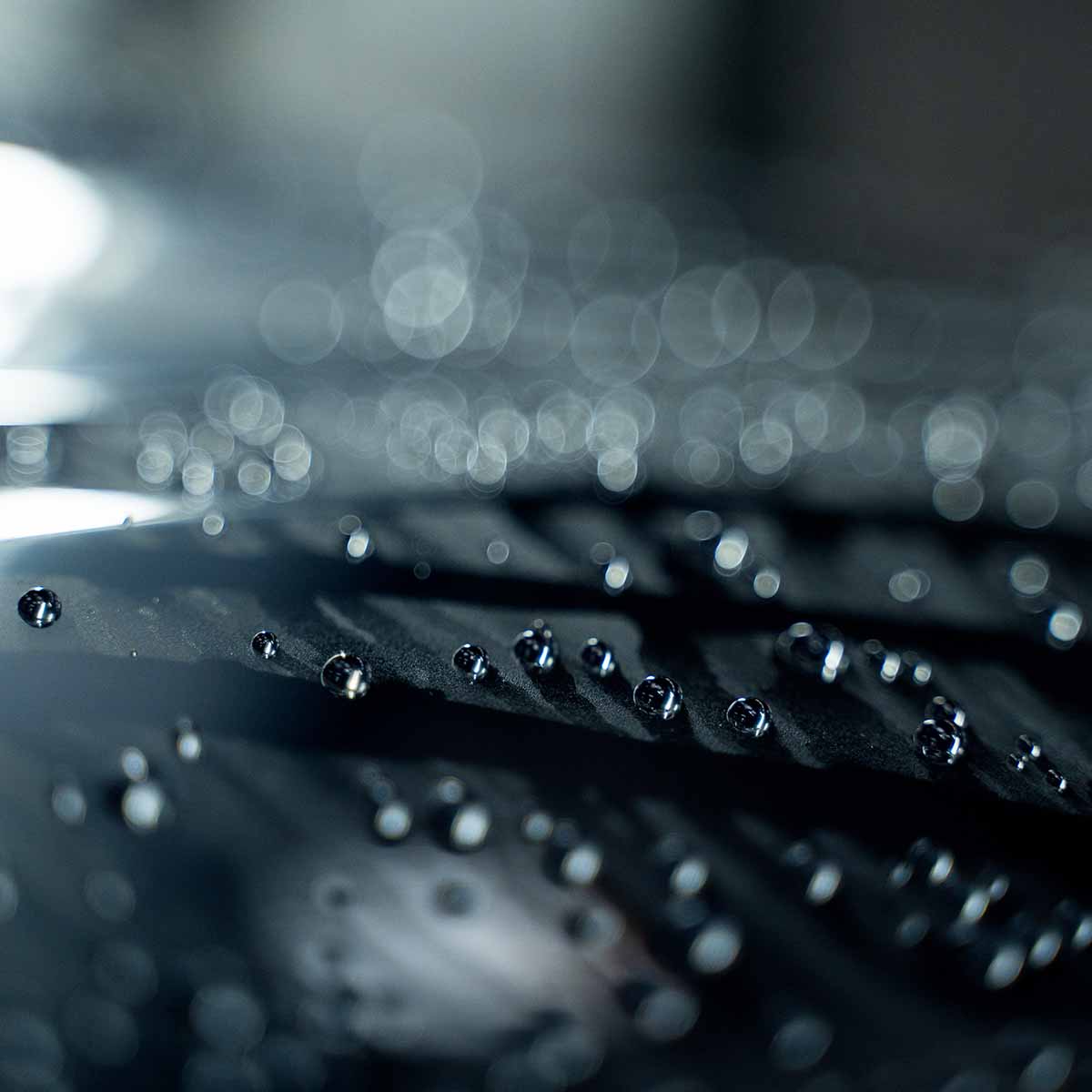 A close-up macro shot of round, tight water beads on a dark car surface, demonstrating the hydrophobic effect of Labocosmetica Revitax.